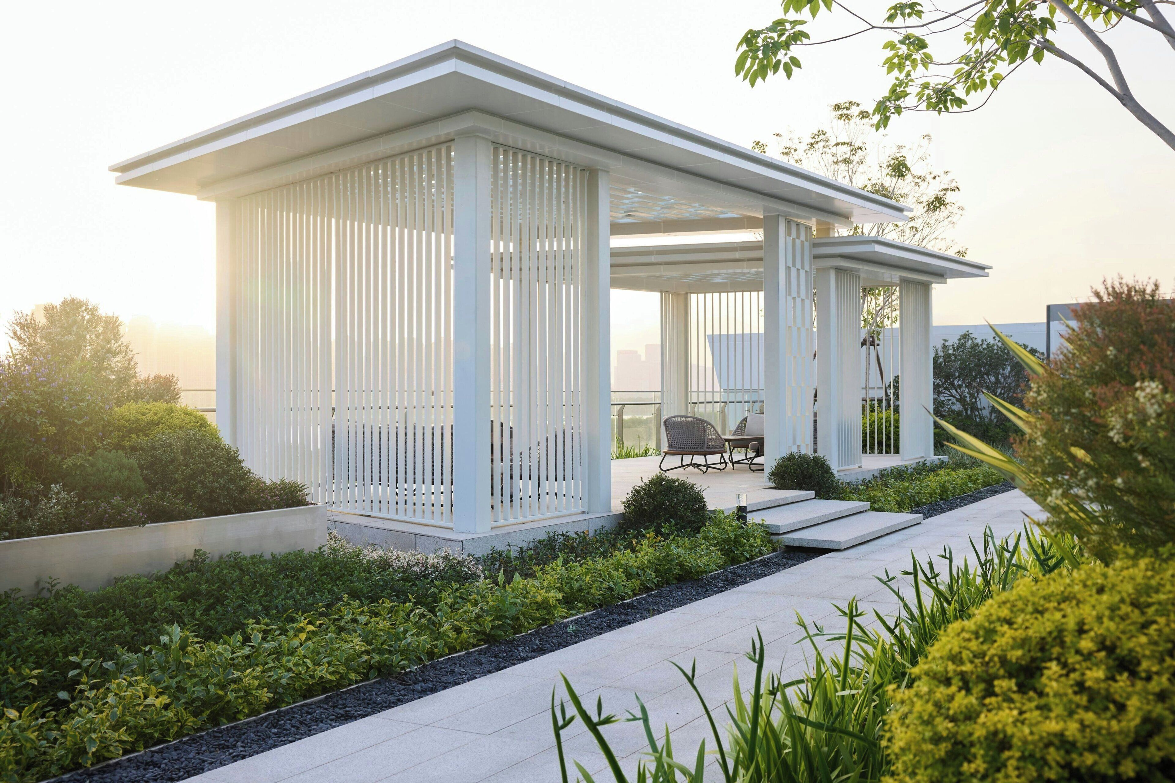 Una casa moderna con un porche cubierto, un jardín con diversas plantas y una zona de estar con mesa y sillas.
