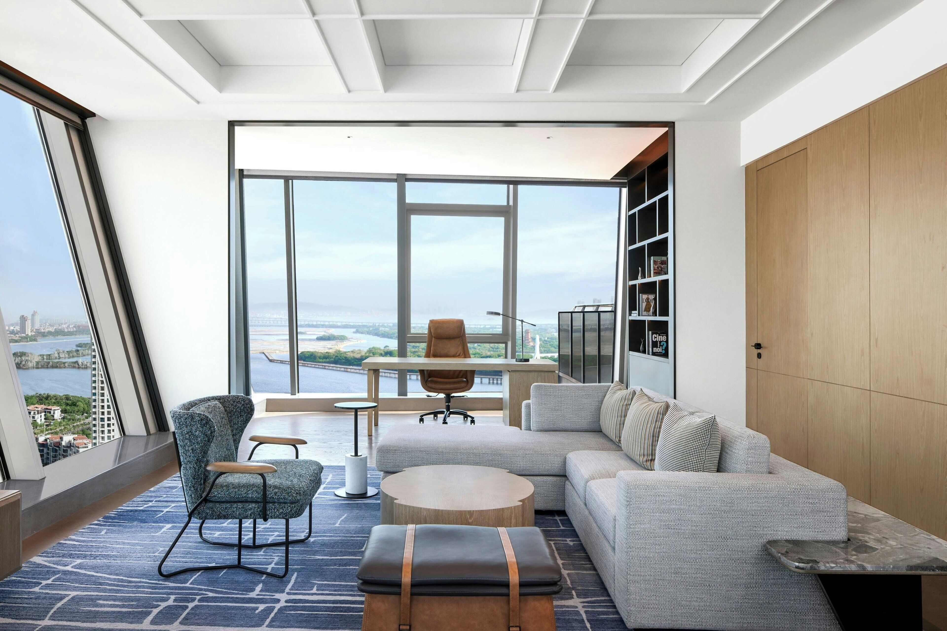 A modern living room with a large window, a sofa, a chair, a coffee table, and a wooden cabinet.