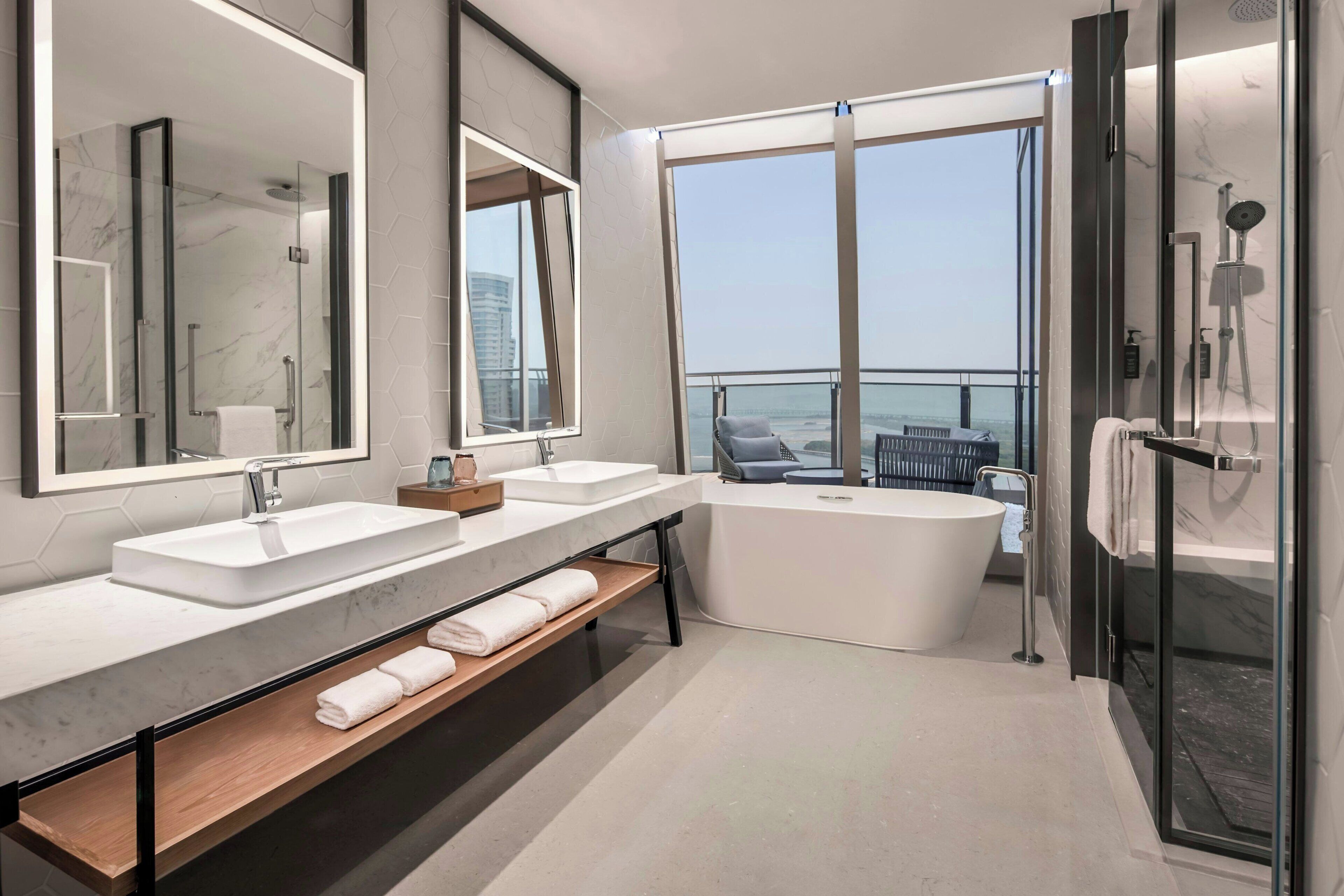 A modern bathroom with a large bathtub, two sinks, and a glass-enclosed shower area.