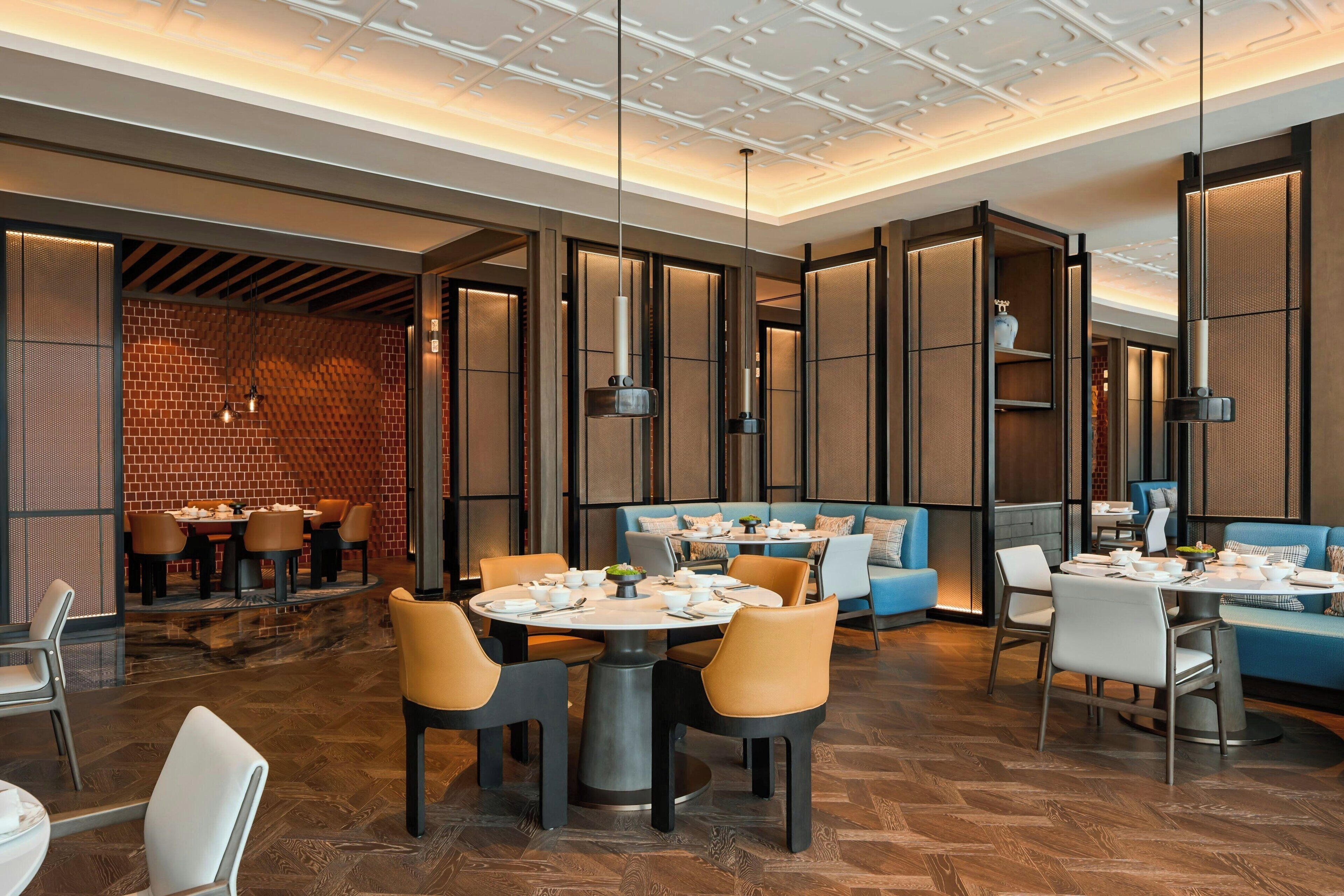 Un restaurante moderno con mesas redondas, asientos acolchados e iluminación colgante.
