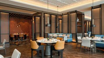 Un restaurante moderno con mesas redondas, asientos acolchados e iluminación colgante.
