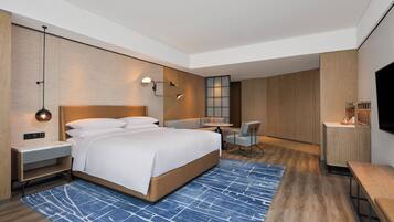 Quarto de hotel moderno com uma cama grande, mesas de cabeceira, escrivaninha e televisão.