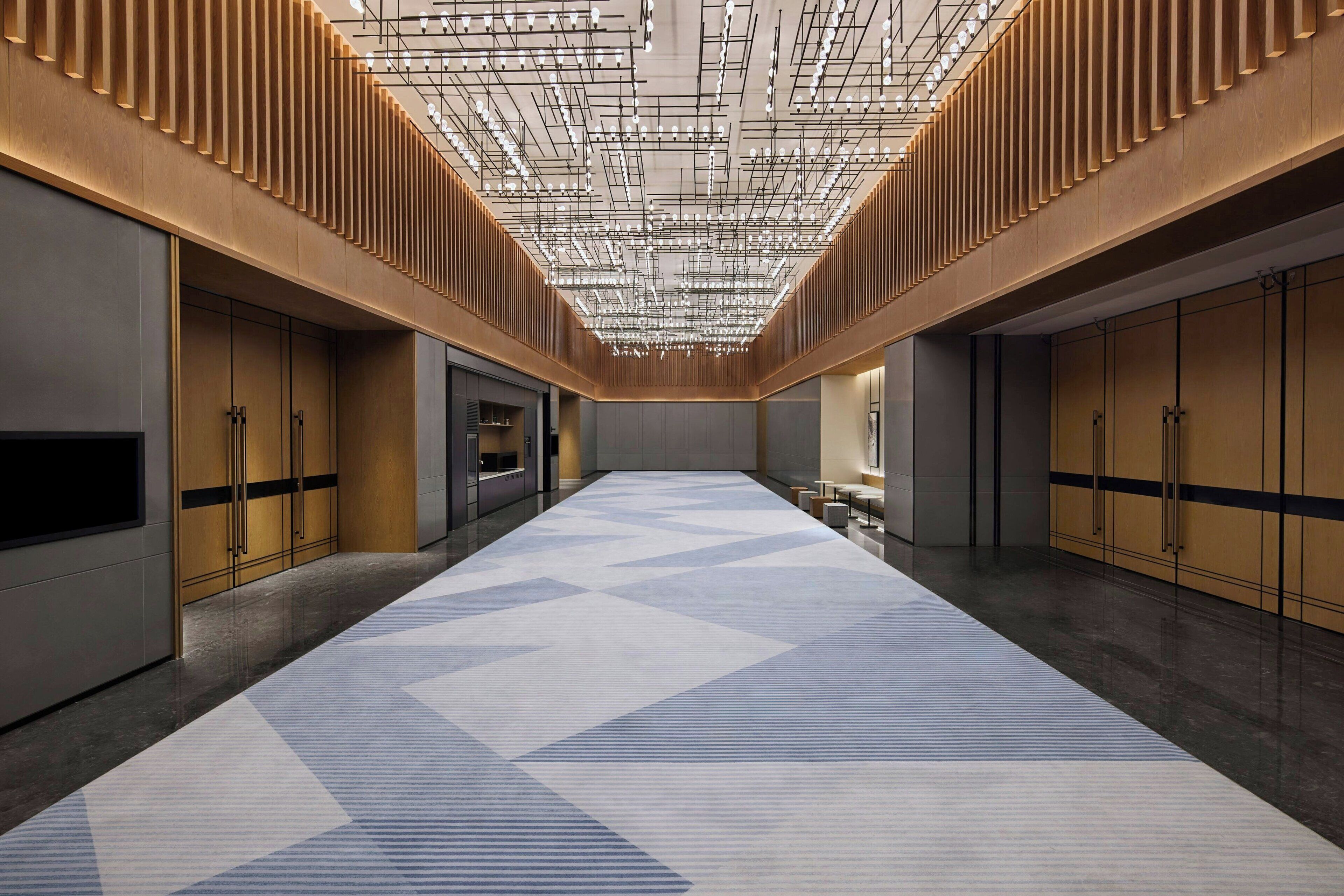 A spacious hallway with a geometric patterned carpet, wooden paneling on the walls, and a ceiling with exposed lighting fixtures.