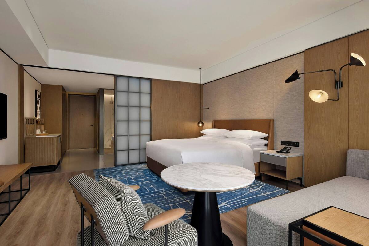 Ein modernes Hotelzimmer mit Bett, rundem Tisch, Sofa, Schreibtisch und Nachttisch.