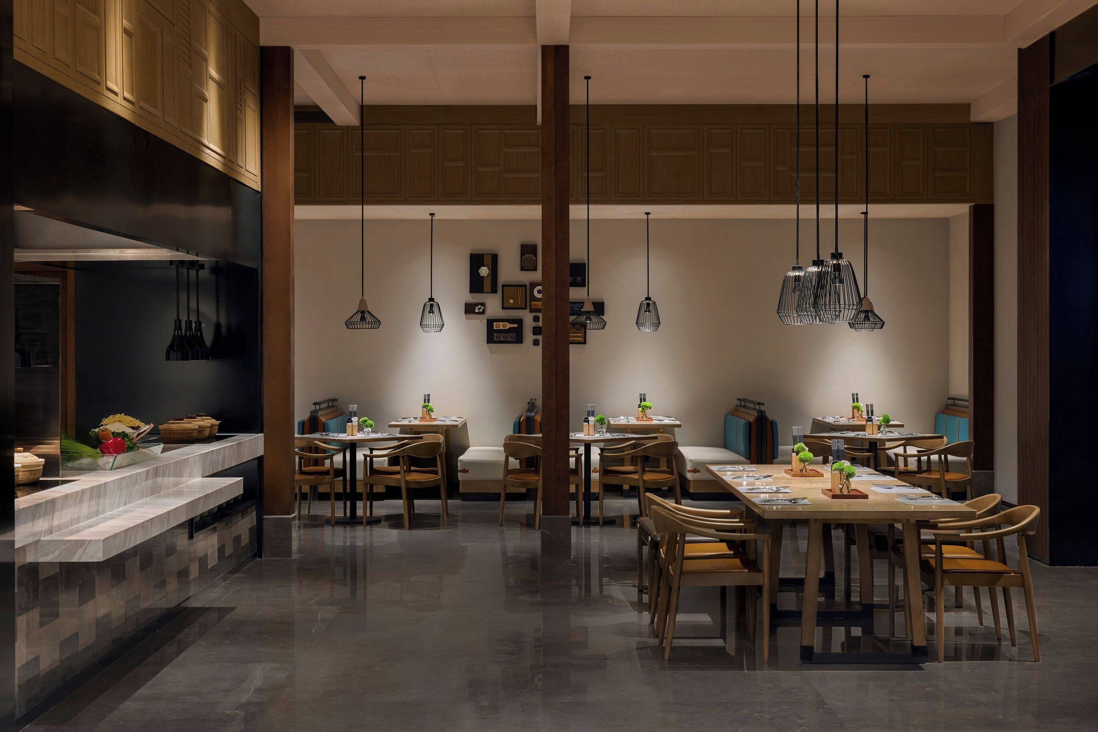 A modern dining area with multiple tables and chairs, wooden cabinets, and pendant lighting.