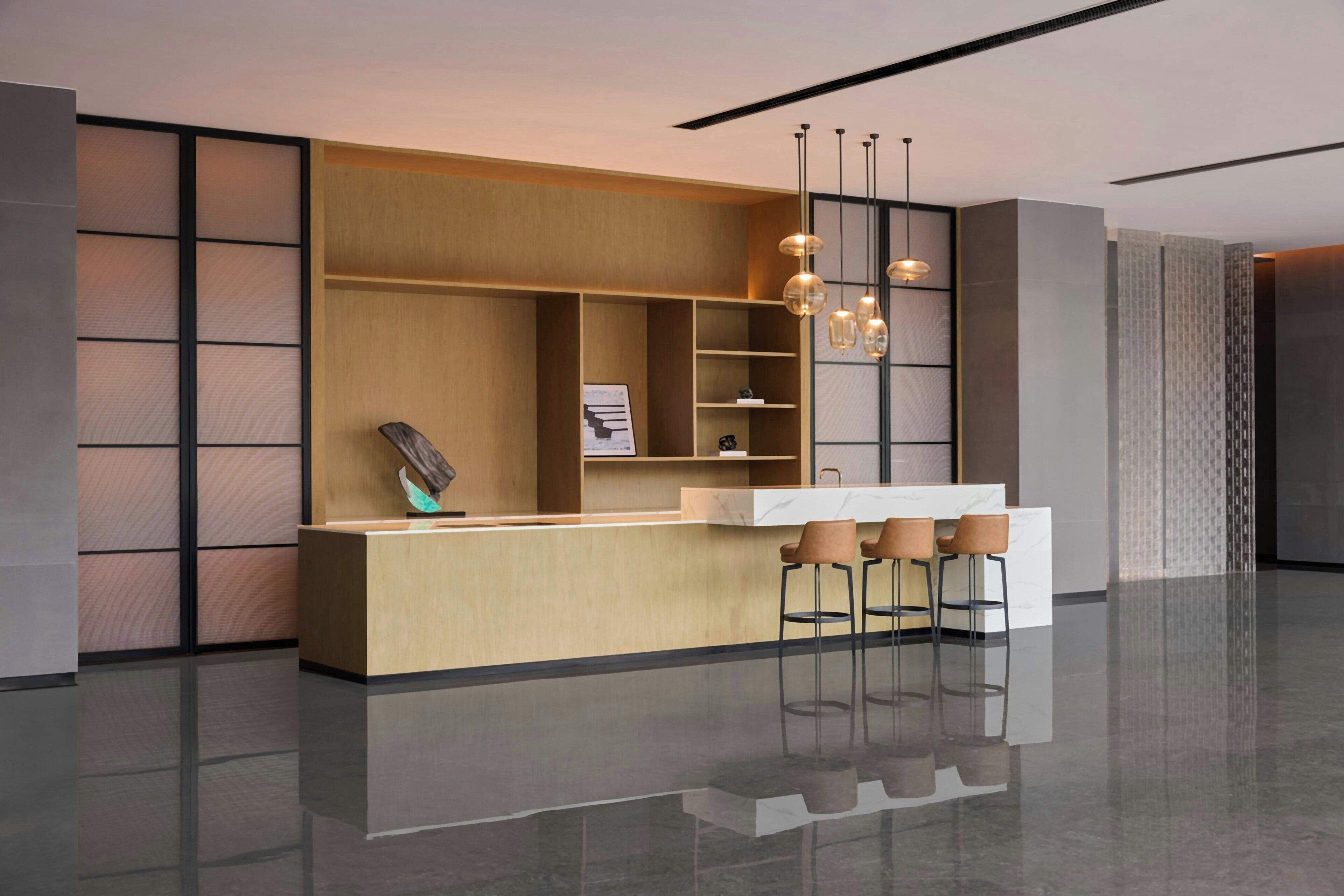 Ein moderner Empfangstresen mit minimalistischem Design, mit einer Holzvertäfelung im Hintergrund, einer weißen Marmorplatte und drei Barhocker.
