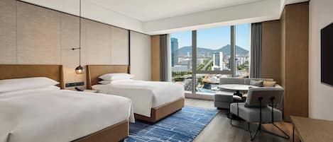 Habitación de hotel con dos camas, un sofá, una mesita y vista a la ciudad.