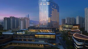 A modern hotel with a curved glass facade, surrounded by other high-rise buildings. - Sheraton Grand Xiamen Jimei (Xiamen)