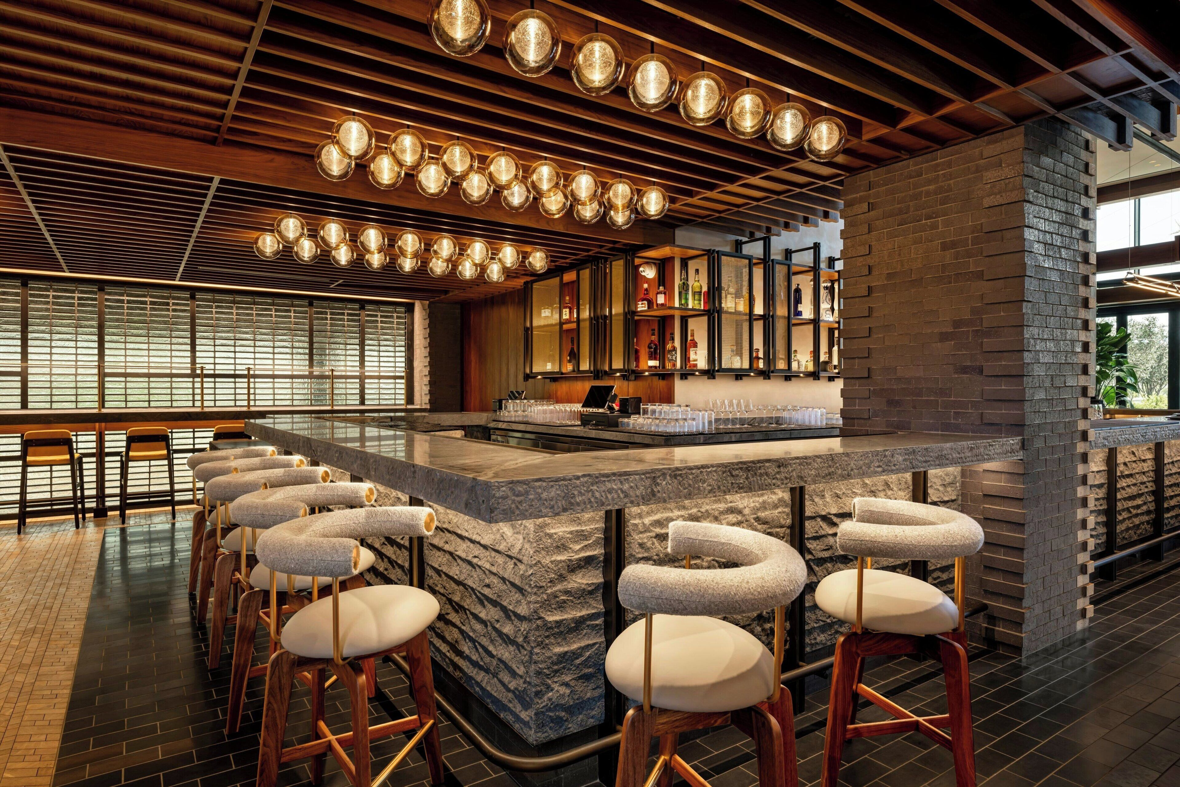 A bar area with a stone counter, multiple stools, and hanging spherical lights.