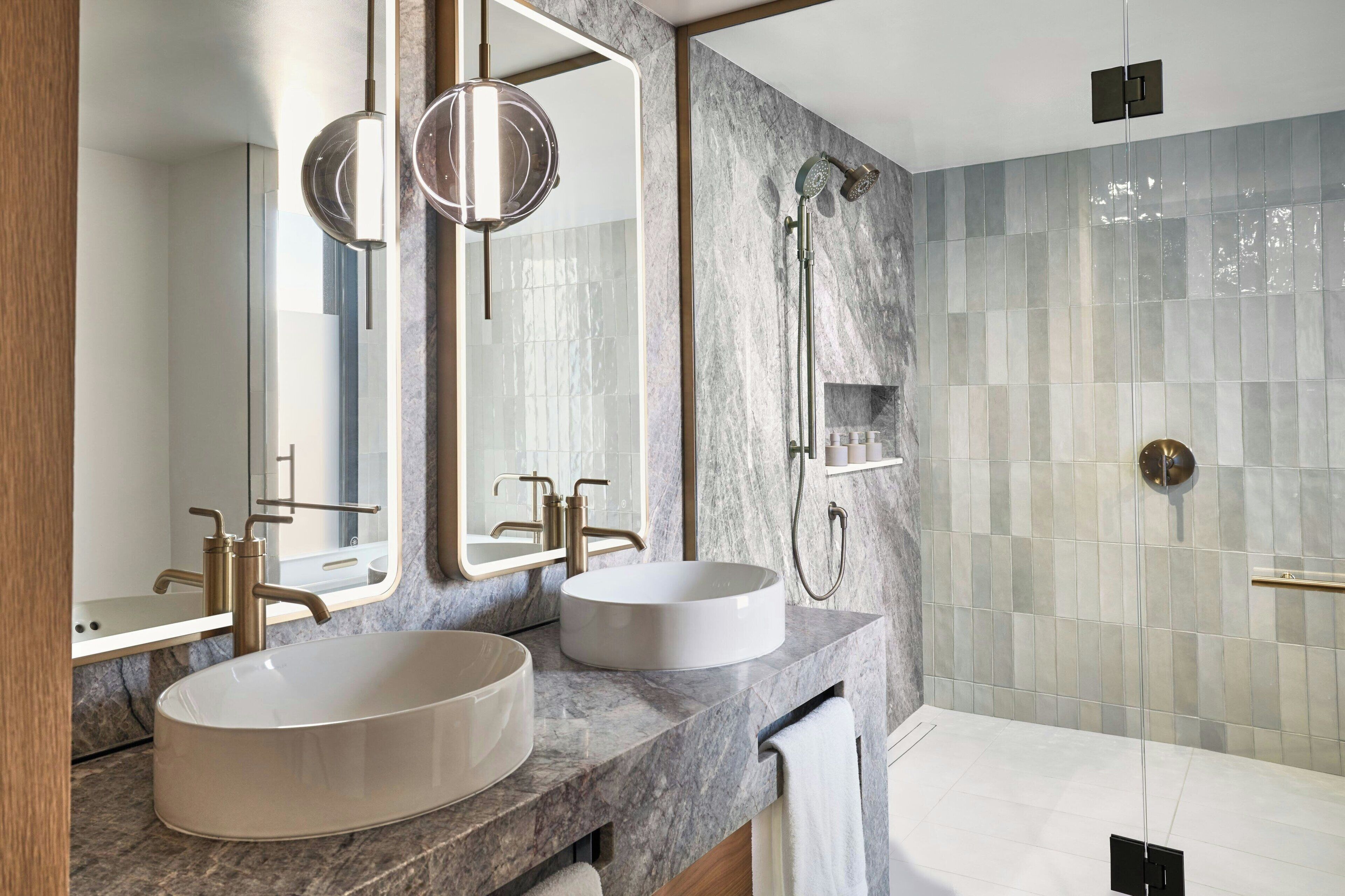 A modern bathroom with two sinks, a large mirror, and a shower.