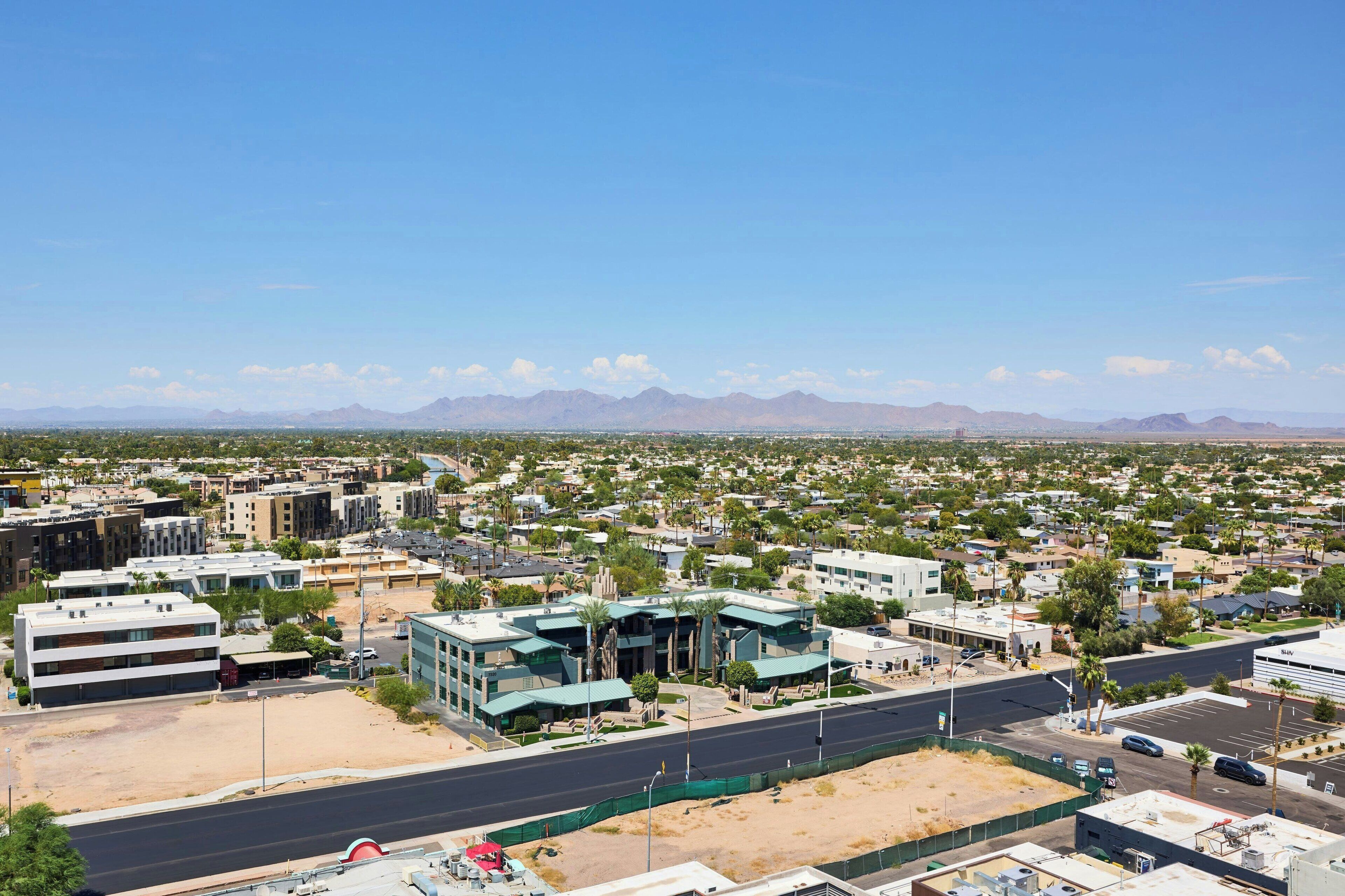 A cityscape with modern buildings, a wide road, and distant mountains.
