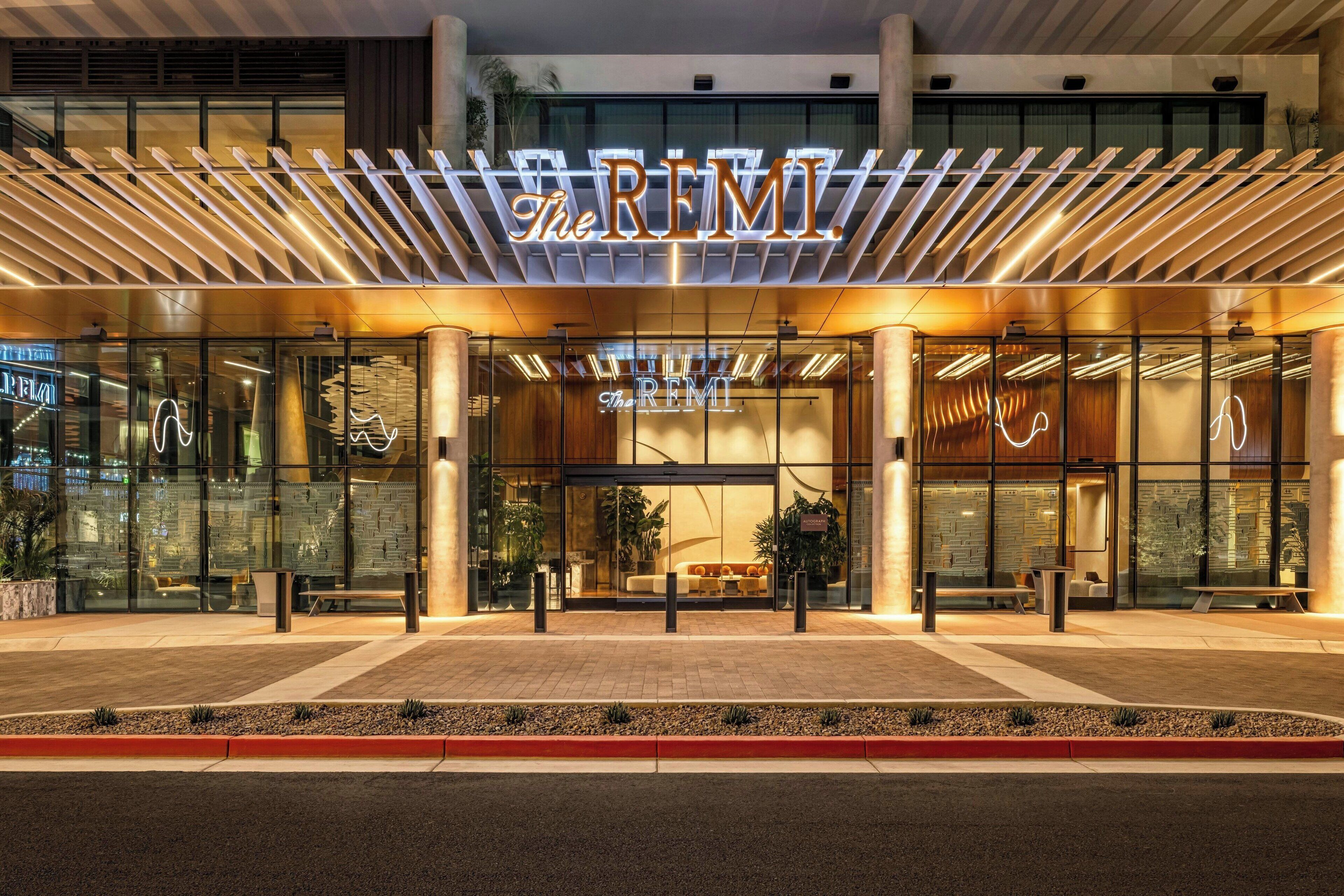 A modern hotel entrance with a prominent sign, glass doors, and a seating area outside.