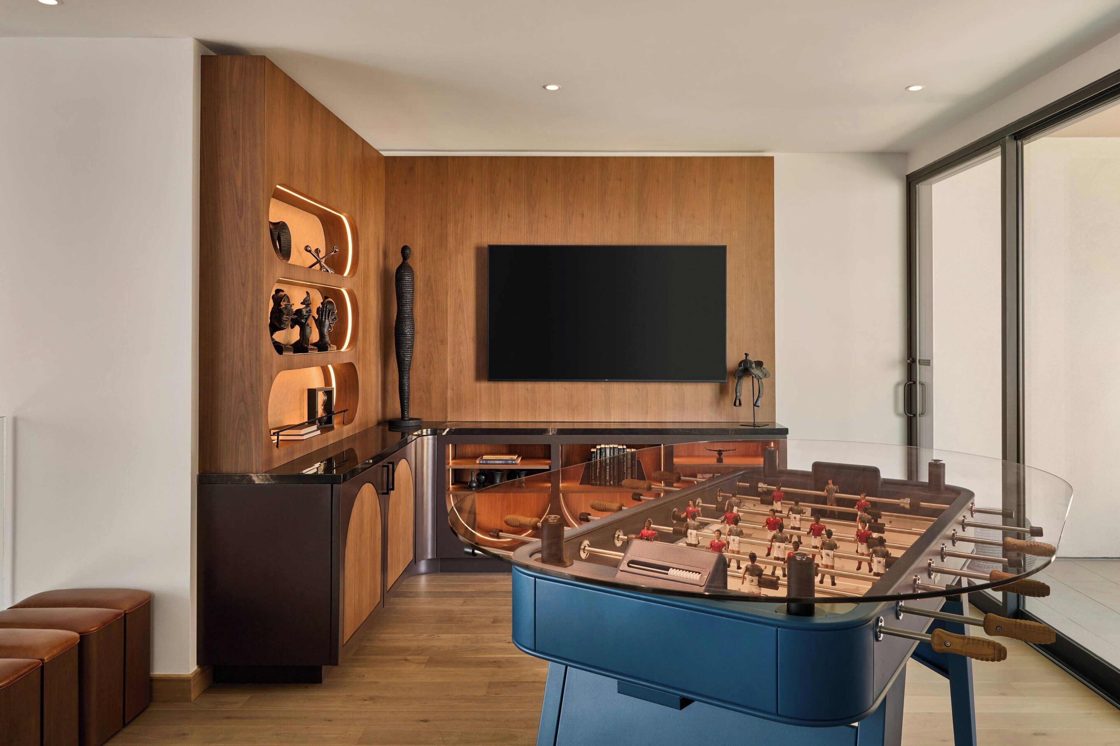 A modern kitchen with a foosball table, wooden cabinetry, and a large flat-screen TV.