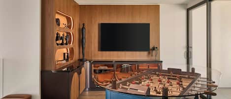 A modern kitchen with a foosball table, wooden cabinetry, and a large flat-screen TV.