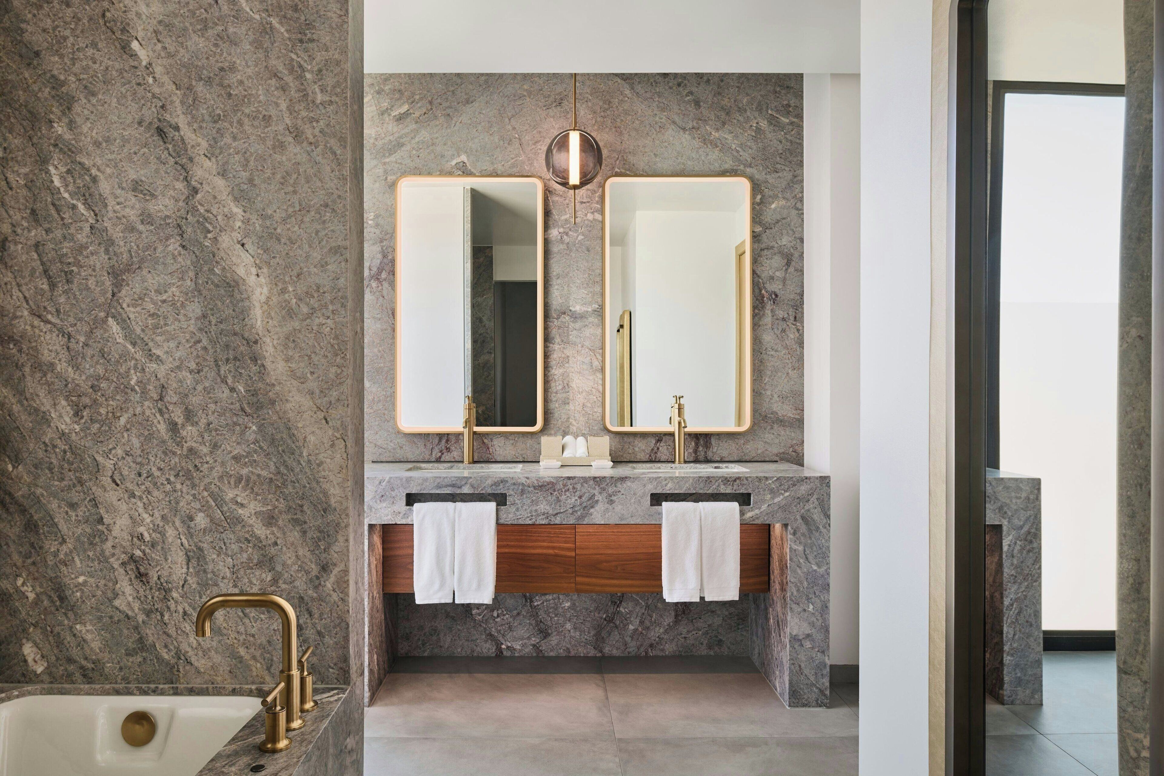 A modern bathroom with marble walls, dual sinks, and a large mirror.