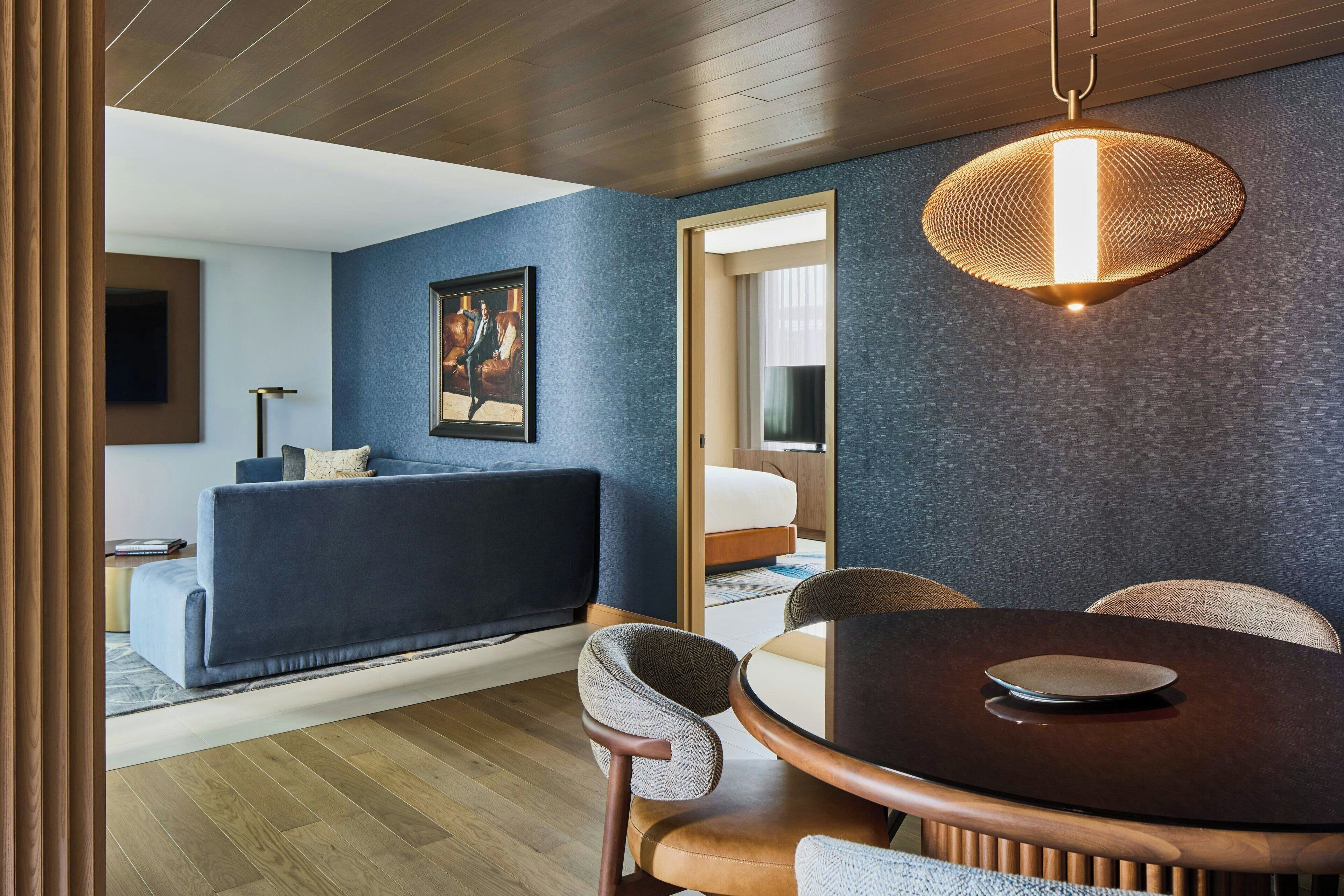 A modern living room with a dark blue sofa, a round dining table, and a unique textured hanging light fixture.
