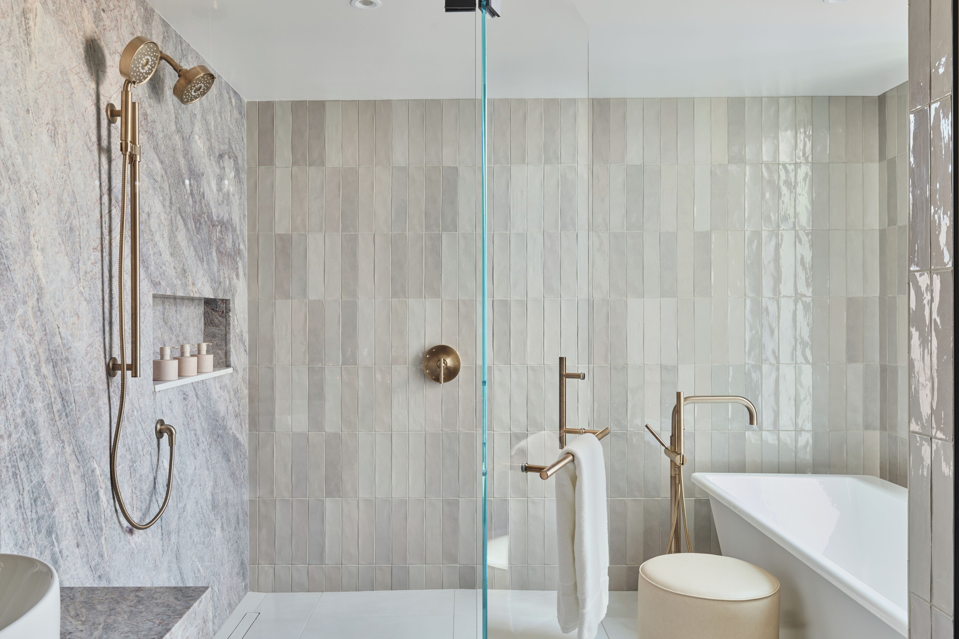 Un baño moderno con ducha envuelta en vidrio, una bañera independiente y paredes de mármol.