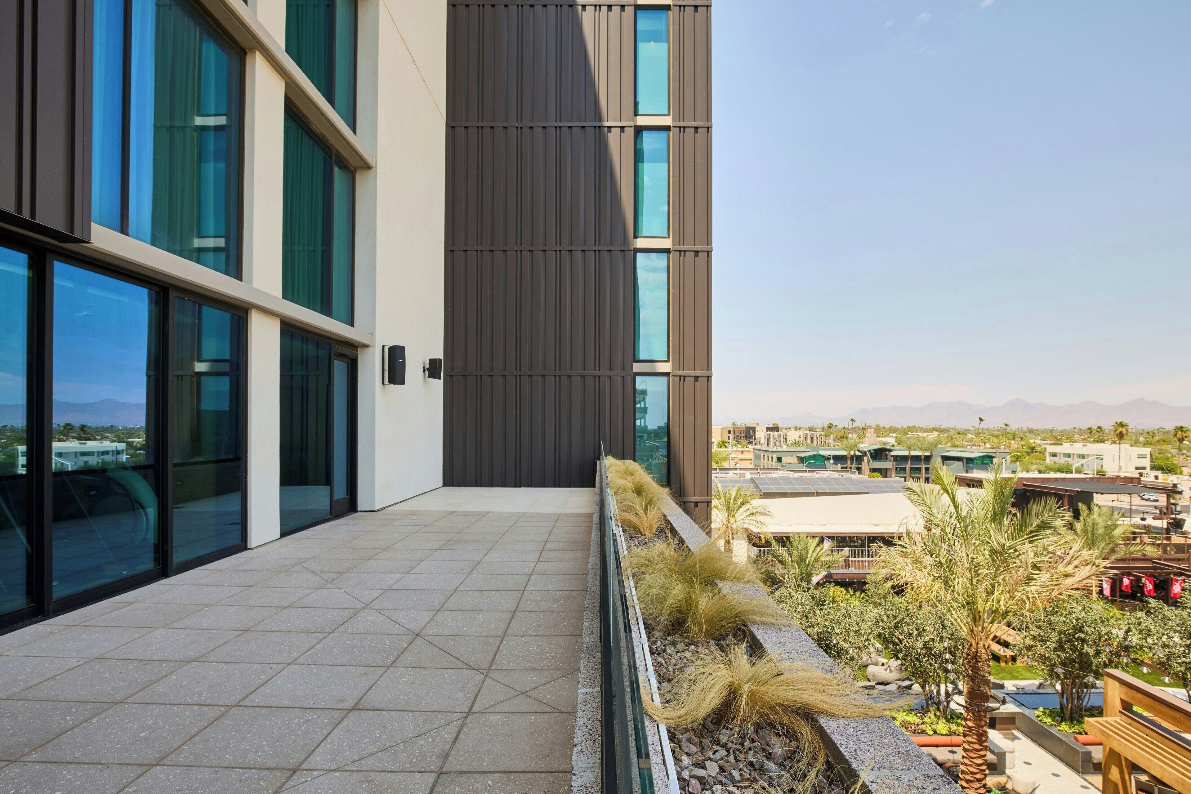 Un edificio moderno con ventanas amplias, una terraza con baldosas y vistas del entorno.