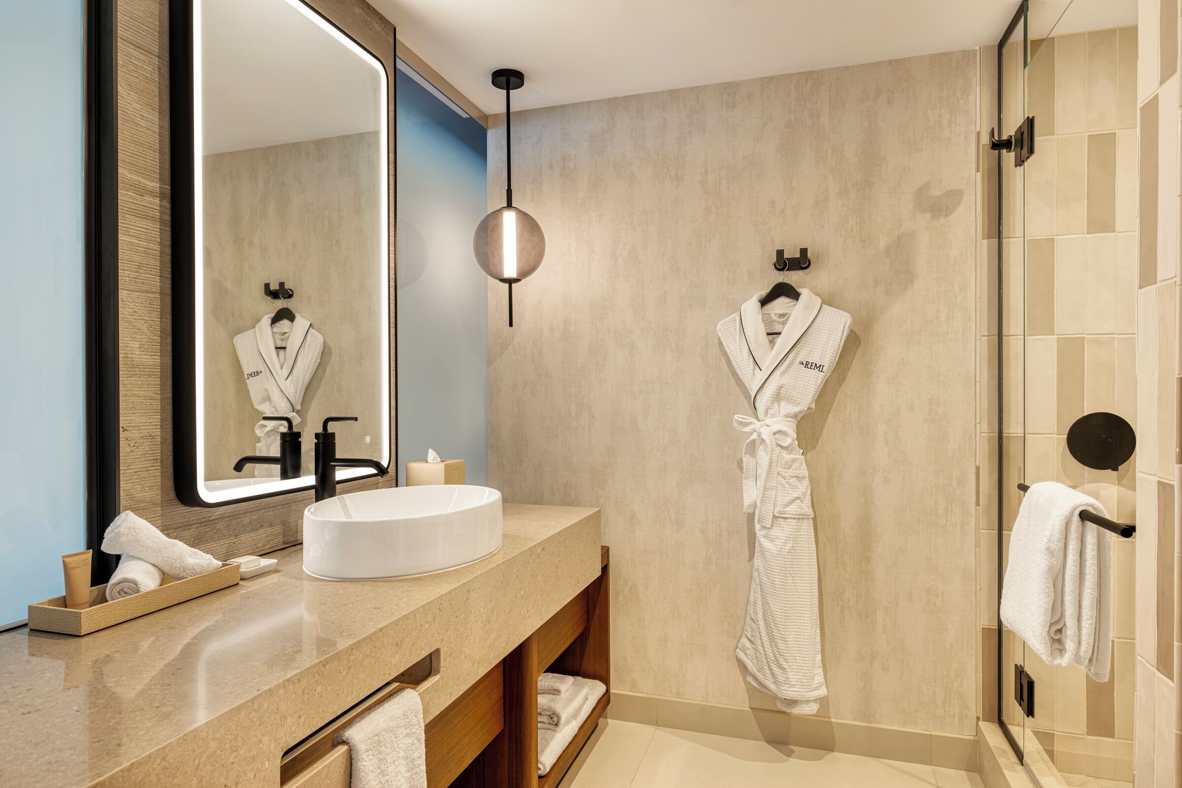 A modern bathroom with a round sink, a large mirror, and a robe hanging on the wall.