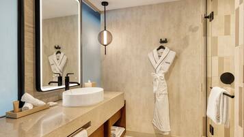 A modern bathroom with a round sink, a large mirror, and a robe hanging on the wall.