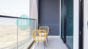 A balcony with two wicker chairs, a glass door, and a view of a road. - Bloomfields Modern 1Br Bingahtti Onyx (Dubai)