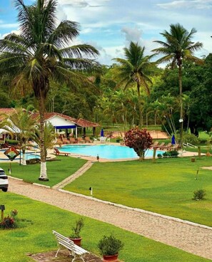 A resort with a swimming pool, palm trees, and a covered seating area. - Hotel Fazenda Cachoeiras de Cavaru (Vassouras)
