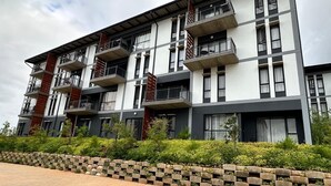 Un edificio de varios pisos con balcones, un camino de ladrillo y áreas verdes al frente.