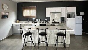Una cocina moderna con una isla central, taburetes de bar, lavavajillas, estufa y refrigerador.