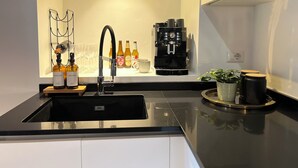 Et moderne køkken med en sort vask, kaffemaskine og en bordplade med flasker og glas.
