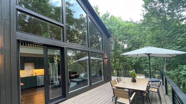 Een modern terras met een eettafel en stoelen, een grote parasol en uitzicht op het omliggende groen.