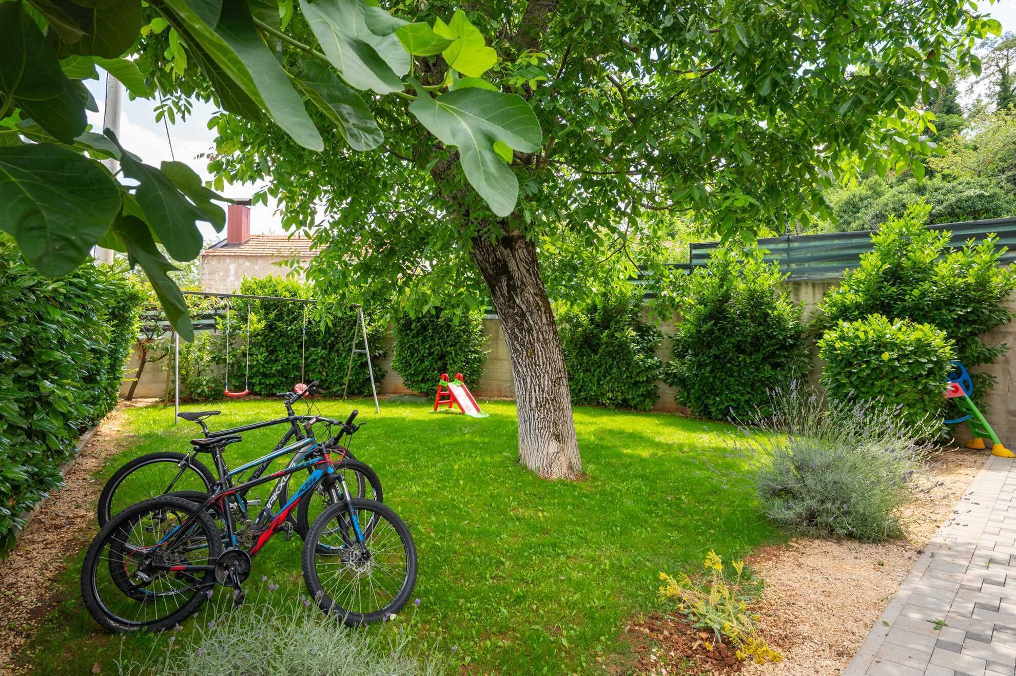 A garden with a swing set, a bicycle, and a tree.