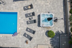 An aerial view of a pool area with a hot tub, lounge chairs, and a small garden.