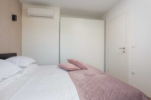 Een slaapkamer met een bed, kussens, een airconditioner, een kledingkast en een deur.