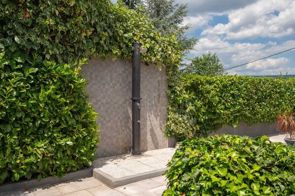 Een tuin met een betegelde muur, een metalen paal en weelderige groene beplanting.