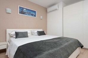 A bedroom with a bed, pillows, a nightstand, a wall-mounted air conditioner, and a framed picture.