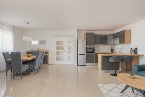 Een moderne keuken met een koelkast, oven en magnetron. Er is een eethoek met een tafel en stoelen.