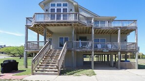 Une maison de deux étages située en bord de mer, dotée d’un balcon à chaque étage, d’un escalier reliant les niveaux et offrant une vue dégagée sur la plage.