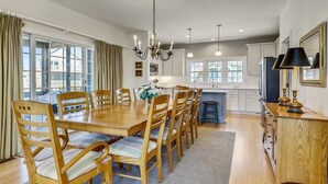 Un coin repas avec une table et des chaises en bois, un lustre et une vue sur l’extérieur grâce à de grandes fenêtres.