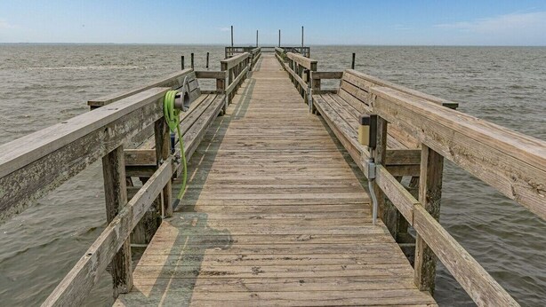 Une jetée en bois s’étendant sur des eaux calmes, sous un ciel dégagé.