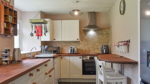 A compact kitchen with white cabinets, a built-in oven, a microwave, and a coffee maker. There are two white chairs and a small table. - 4 bedroom accommodation in Carmarthen (Carmarthen)