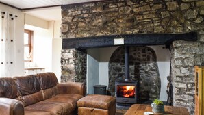 A cozy living room with a stone fireplace, leather sofa, and a wooden coffee table. - 4 bedroom accommodation in Carmarthen (Carmarthen)