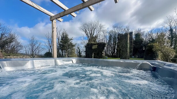 A hot tub with a wooden pergola overhead, surrounded by trees and stone walls. - 4 bedroom accommodation in Carmarthen (Carmarthen)