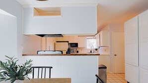 A compact kitchen with white cabinets, a wooden countertop, and a dining area with a table and chairs.