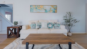A living room with a white sofa, a wooden coffee table, and a large abstract painting on the wall.