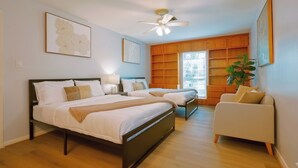 A bedroom with two beds, a ceiling fan, wooden shelving, a plant, and a white sofa.