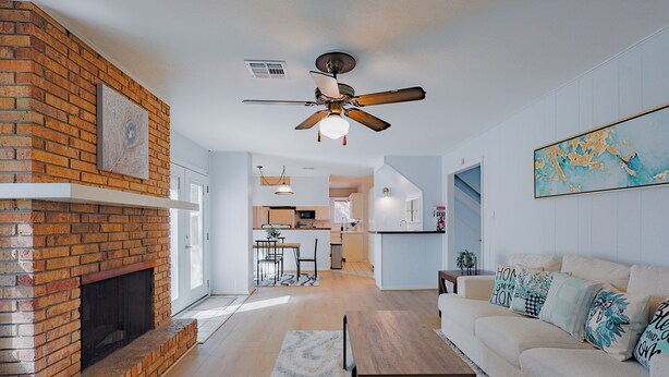 A living room with a brick fireplace, a ceiling fan, and a sofa with decorative pillows.