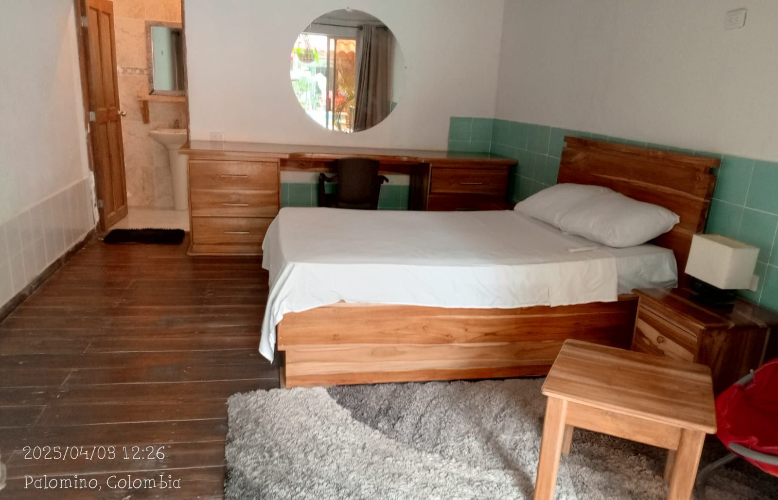 Un dormitorio con una cama de madera, una mesita de noche pequeña, un espejo y una ventana con vistas al exterior.