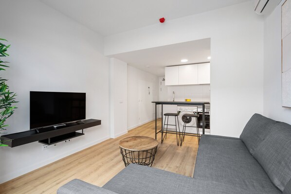 A modern living room with a flat-screen TV, grey sofa, and a small round table.