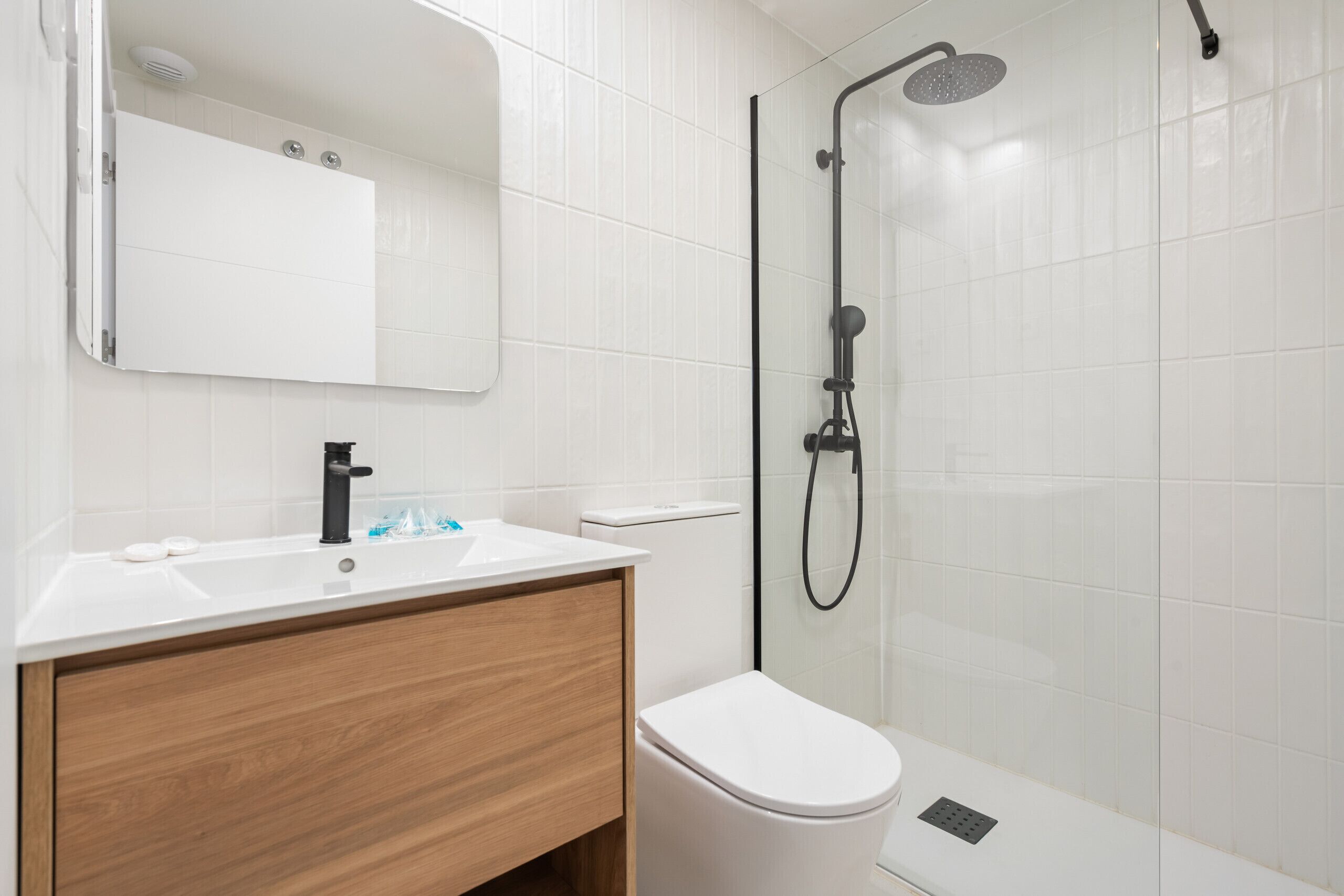 A modern bathroom with a white sink, wooden vanity, a toilet, and a glass-enclosed shower area.