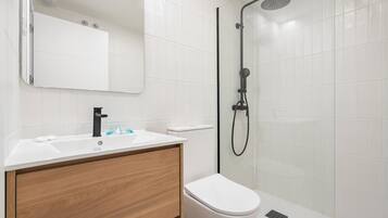 A modern bathroom with a white sink, wooden vanity, a toilet, and a glass-enclosed shower area.